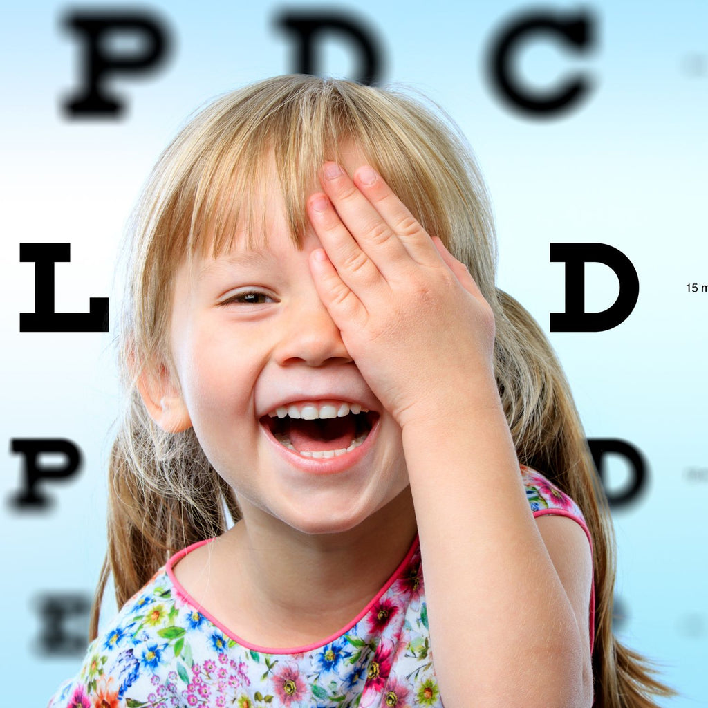 Girl holding eye while getting eye exam with Snellen Chart in the background