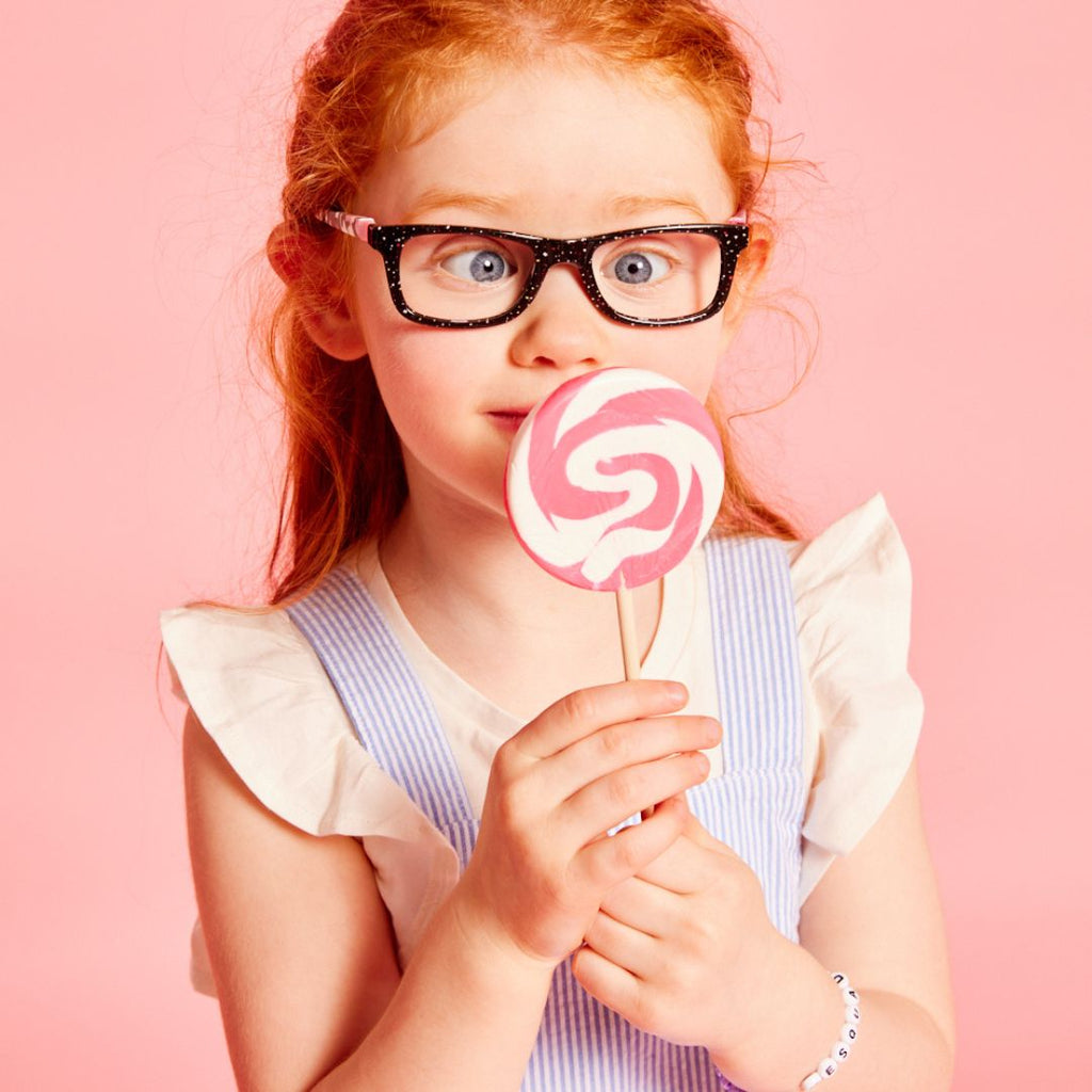 Cute young girl wearing black glasses, looking cross-eyed at a lollipop | MEsquad Kids